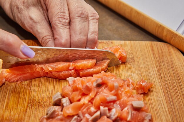 Chefs Hands Cutting Fresh Salmon Fillet with Knife on Wooden Cutting Board in Kitchen