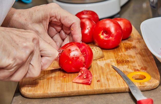 写真 キッチンの木製のカッティングボードで新鮮なトマトを切るシェフの手