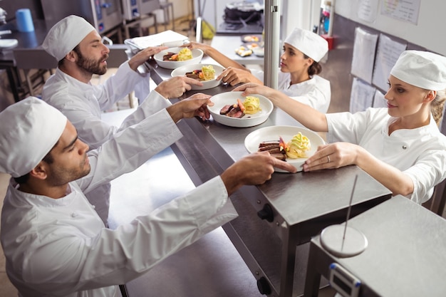 Chefs passing ready food to waiter at order station