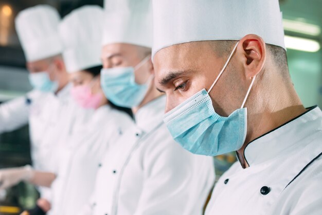 Chef in guanti e maschere protettive preparano il cibo nella cucina di un ristorante o di un hotel.