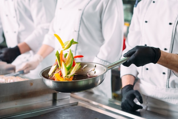 Chefs in protective masks and gloves prepare food in the kitchen of a restaurant or hotel.