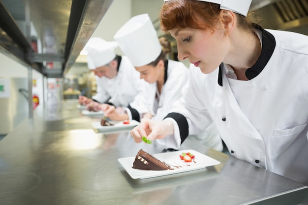 Photo chefs standing in a row garnishing dessert plates