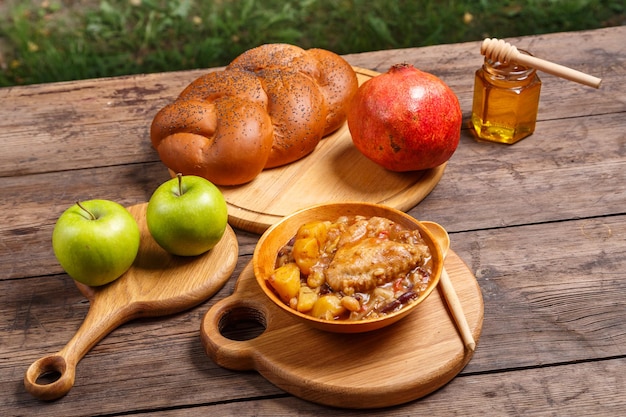 Chelnt with chicken in a wooden plate on the festive table for Rosh Hashanah next to challah honey and apples with pomegranate