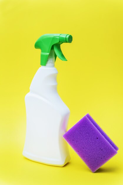 Chemical cleaner in spray and purple sponge on yellow background