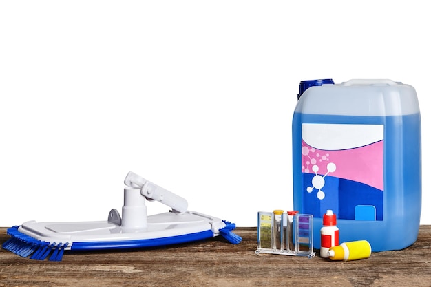 Chemical cleaning product, test tubes, flasks and a big brush for the maintenance of the swimming pool on a wooden surface against a white background. Close-up front view. Disinfectant, detergent, cle