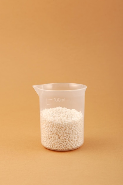 Chemical fertilizer in plastic measuring cup. Small white balls. Agricultural economics.
