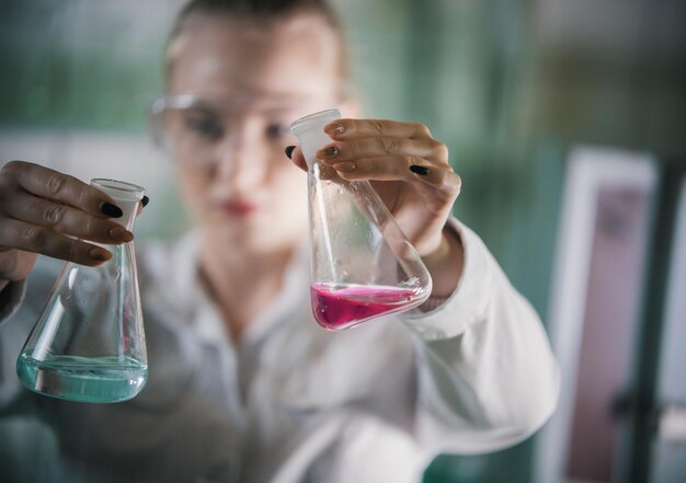 Chemical laboratory young blonde woman holding a flasks with pink and blue liquid in it