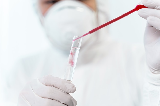 Chemical reaction. Attentive scientist adding red liquid into test tube and waiting for reaction