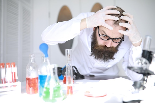 Chemicus gek. Een gekke wetenschapper voert experimenten uit in een wetenschappelijk laboratorium. Doet onderzoek met behulp van een microscoop.