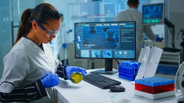 Foto chemicus met beschermingsglas die verschillende bacteriën onderzoekt die petrischaaltje vasthouden in laboratorium typen op pc. artsen die de evolutie van het vaccin analyseren met behulp van hightech onderzoek naar de diagnose tegen het covid19-virus.