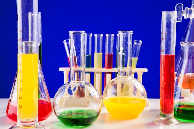 Chemie lab set met gekleurde vloeistoffen op een tafel op blauwe achtergrond. glaswerk en biologie apparatuur