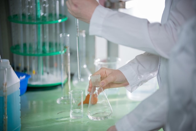 Chemisch laboratorium jonge vrouw die een kolf vasthoudt, transfuseert iets met behulp van een pipet