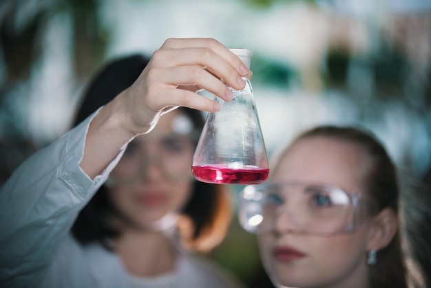 Chemisch laboratorium twee jonge vrouwen met een kolf met roze vloeistof erin kolf in focus