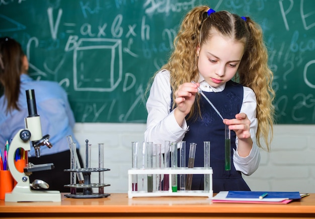 Chemische analyse Schoolleerling bestudeert chemische vloeistoffen Scheikundeles op school Reageerbuisjes met stoffen Laboratoriumglaswerk Schoollaboratorium Meisje slimme student voert schoolexperiment uit