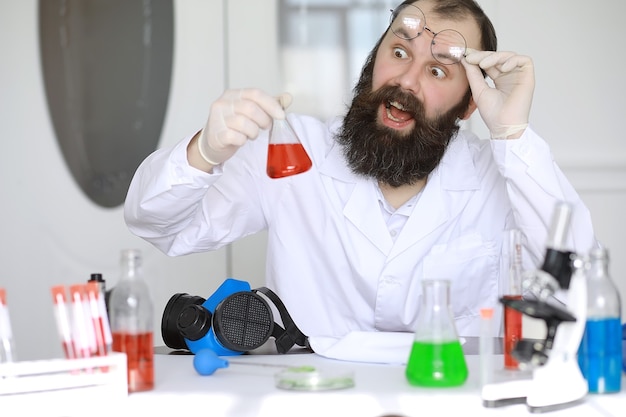Химик сумасшедший. Сумасшедший ученый проводит эксперименты в научной лаборатории. Проводит исследования под микроскопом.