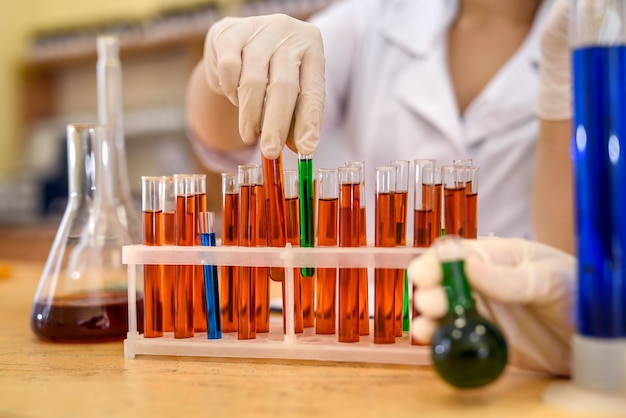 Chemist rack with test tubes of red color and human hands in protective gloves