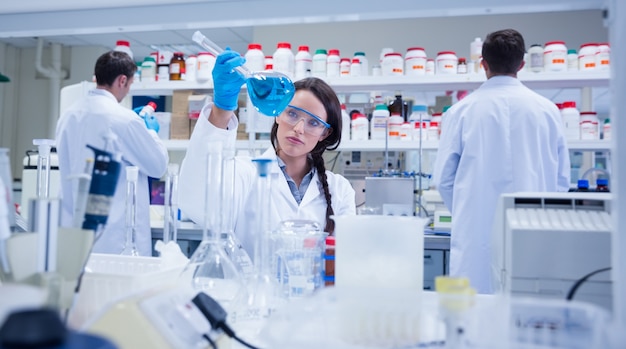 Chemist raising beaker of blue liquid with colleagues behind