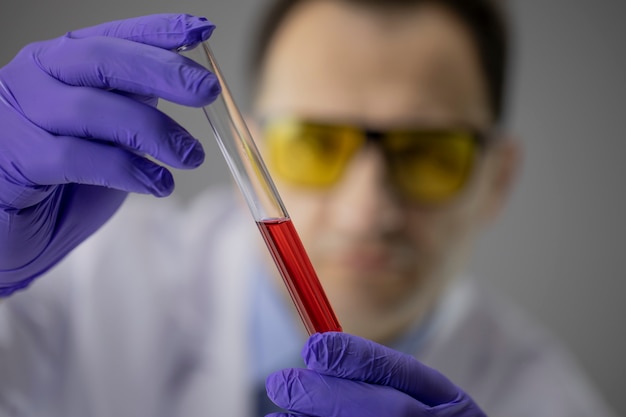 Chemist researcher in blue gloves holding test tube with transparent red liquid