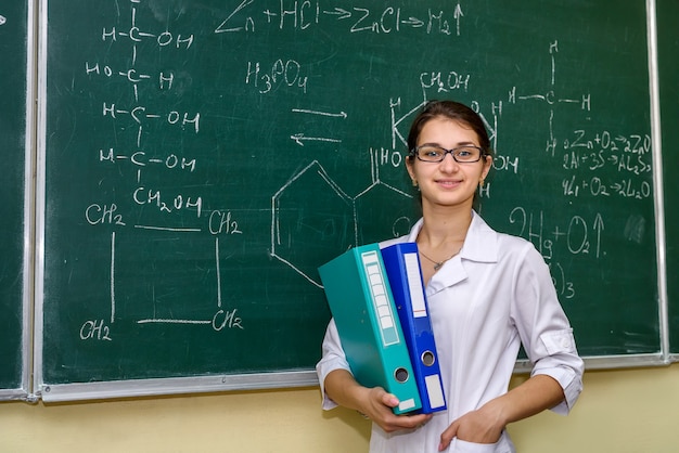 Chemist with folders standing and posing. Behind woman university board with chemical formulas