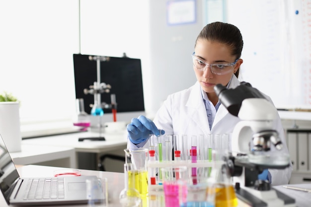 Chemist woman holding test tube with liquid in front of microscope in laboratory