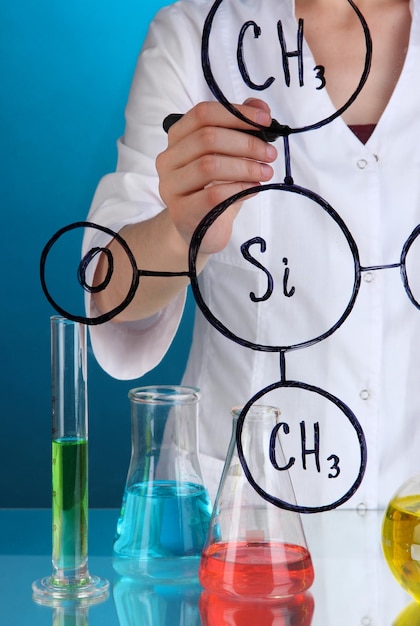 Chemist woman writing formulas on glass on blue background