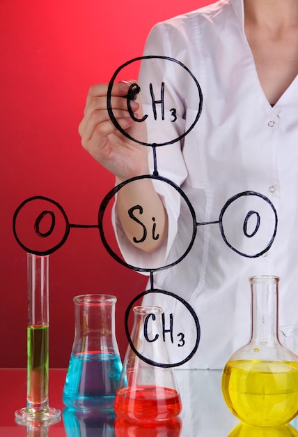 Chemist woman writing formulas on glass on red background