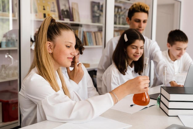 Фото Урок химии школьница и одноклассники держат колбу для экспериментов и улыбаются в лаборатории школьное образование