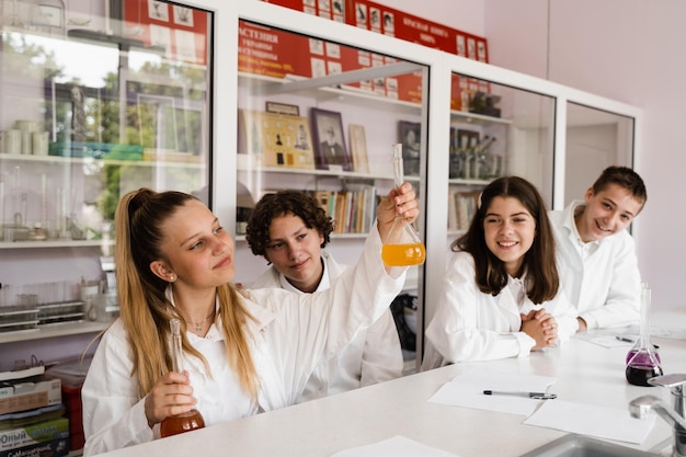 화학 수업 여학생과 급우들은 실험실 학교 교육에서 실험과 미소를 위해 플라스크를 들고 있습니다.
