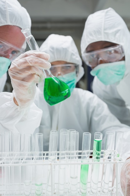  Chemists in protective suits looking at green liquid in beaker