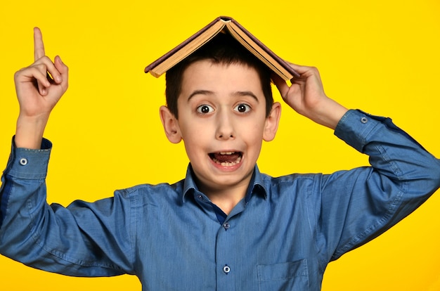 Cherful boy with a book on his head on yellow background