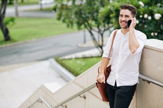 cherful young man standing outdoors and answering phone call from friend or family member