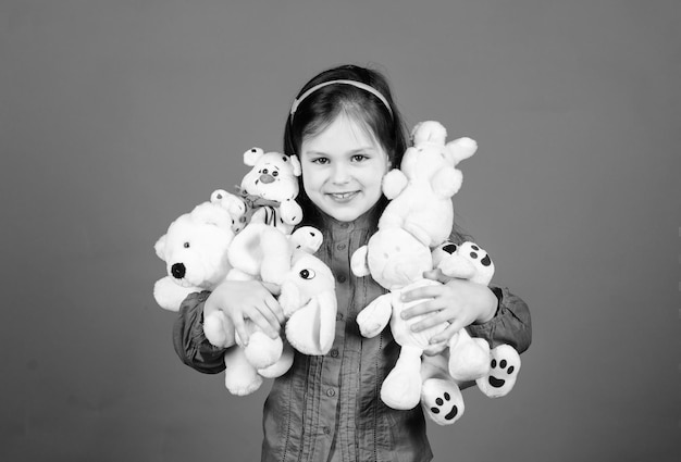 Фото Улыбающееся лицо маленькой девочки с игрушками счастливое детство маленькая девочка играет с мягкой игрушкой плюшевым медведем много игрушек в ее руках концепция детства коллекционирование игрушек хобби