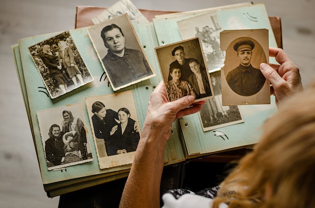 Photo cherkasy/ukraine- december 12, 2019: female hands holding and old photo of her relatives. vintage photo album with photos. family and life values concept.