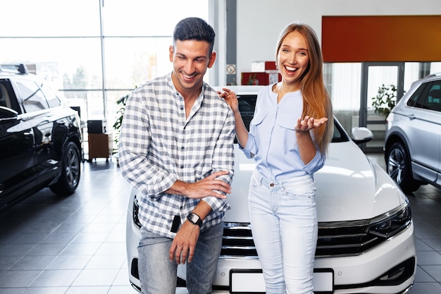 Cherrful young couple at the dealership buying a new car