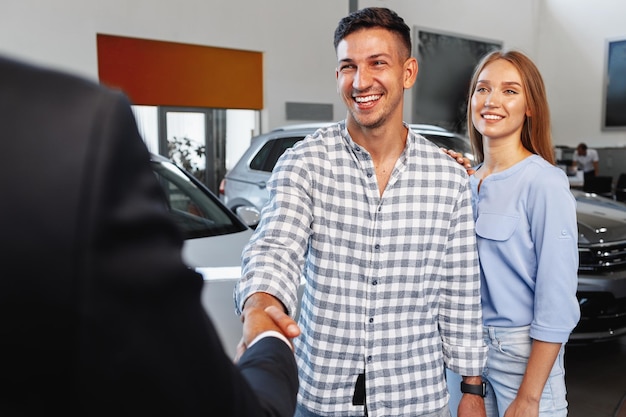 Cherrful young couple at the dealership buying a new car