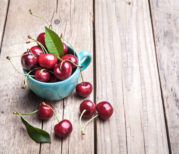 Cherries in the beautiful turquoise cup on wooden table