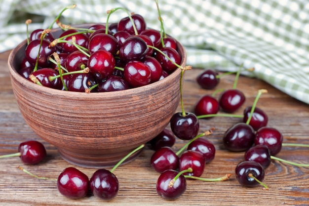 Cherries in the clay bowl on a brown wood table.