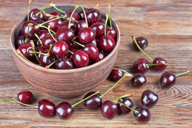 Cherries in the clay bowl on a brown wooden table.