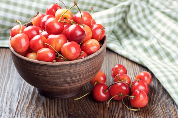 Cherries in the clay bowl on a brown wooden table.