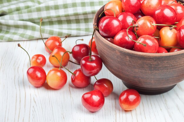 Cherries in the clay bowl on a white wooden table