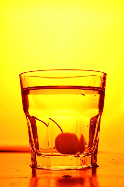 Cherries in a glass on a toned background A bunch of fresh ripe cherries falling into a glass of water with bubbles closeup Refreshing cocktail concept