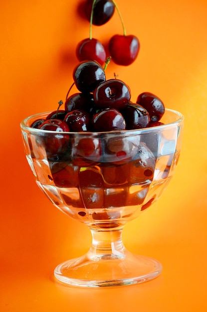 Cherries in a glass vase on orange background