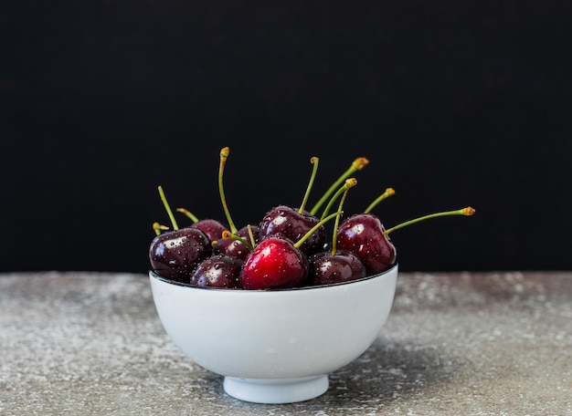 Cherries in white bowl on the table and black background