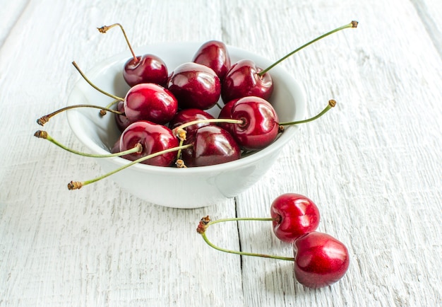 cherries in a white plate on a white wooden table close up