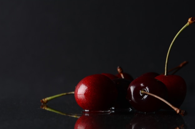 Cherries, with drops of water on a black background with reflection