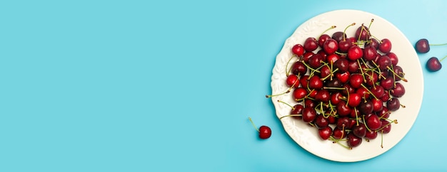 Cherry background. Red juicy sweet cherry on a white plate on a light blue background. Summer fresh juicy berries and food concept.