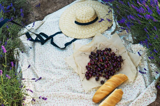 Cherry berries and baguette on the blanket during picnic in the lavender field