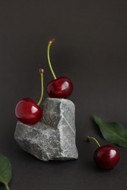 Cherry berries located on a stone in the form of a heart and cherry leaves on a dark background