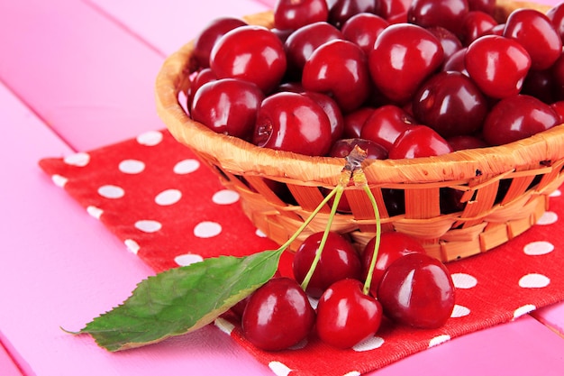 Cherry berries in wicker basket on wooden table closeup