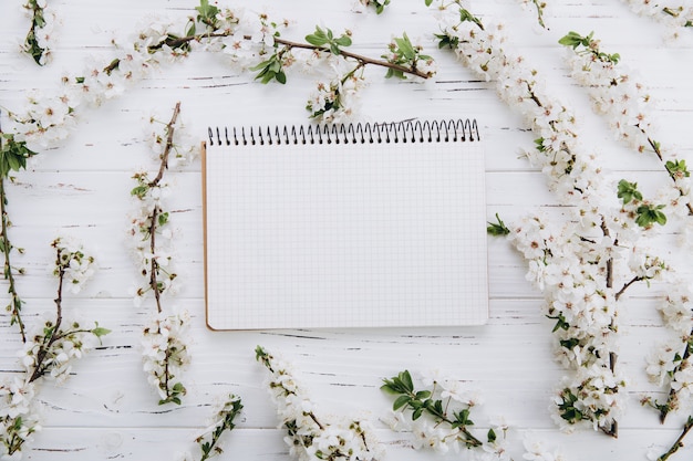 Cherry blossom and empty notebook on white wooden table